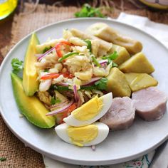 a white plate topped with meat and veggies next to an avocado