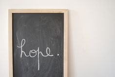 a chalkboard with the word hope written on it in front of a white wall