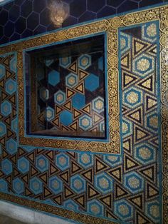 a blue and gold tiled wall with an intricate design in the center, on top of a tile floor