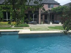 a swimming pool in front of a large house with an outdoor lounge area next to it