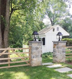 a white shed with two lamps on top of it next to a fence and trees