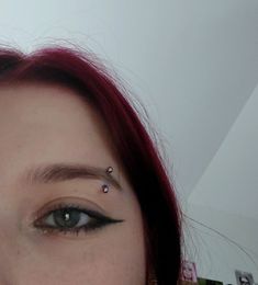 a woman with red hair and piercings on her nose looking at the camera while wearing an earring