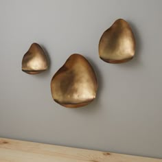 three gold leaf shaped objects mounted to the wall next to a wooden table and gray wall