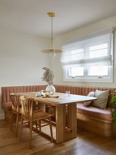 a wooden table sitting under a window next to a bench with two chairs and a vase on it