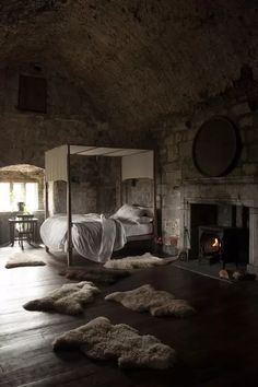 a bedroom with a fireplace and bed in the corner, surrounded by sheepskin rugs