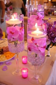 two tall vases filled with pink flowers and lit candles