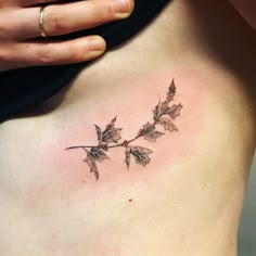 a woman's lower back tattoo with holly leaves and berries on the side ribcage