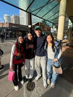 four young people are standing on the sidewalk in front of a bus stop with their arms around each other