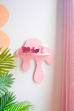 a pink shelf with sunglasses on it next to a potted plant and wall hanging