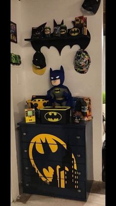 a batman themed dresser in the corner of a room with shelves and decorations on it