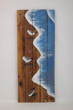 a piece of wood with birds painted on it and the ocean in the back ground