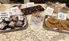 there are many desserts on the table with name tags in front of them, including cookies and brownies