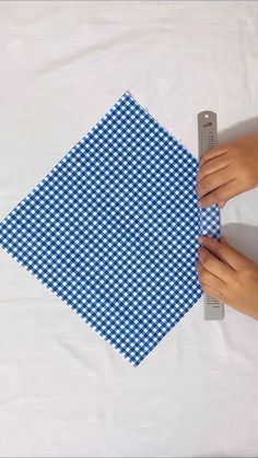 two hands are holding a blue and white checkered piece of cloth on a table