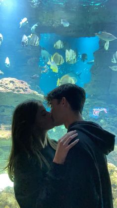 a man and woman are kissing in front of an aquarium with fish swimming around them