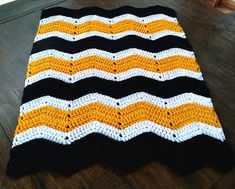 a black, white and yellow crocheted blanket sitting on top of a wooden floor