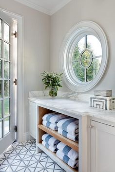 a bathroom with marble counter tops and white cabinets, round window in the wall behind it