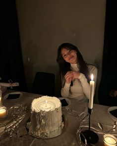 a woman sitting at a table in front of a cake with lit candles on it