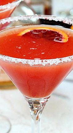 two glasses filled with red liquid and garnished with an orange slice on the rim