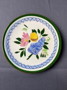 a plate with flowers and leaves painted on the side, sitting on a gray surface