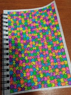 a notebook covered in colorful puzzle pieces on top of a wooden table next to a pen