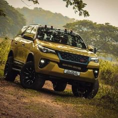 a yellow suv is parked on the side of a dirt road in front of some trees