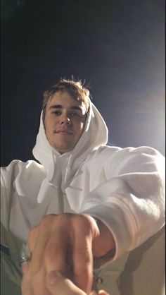 a man dressed in white pointing at the camera with his right arm out and wearing a hoodie