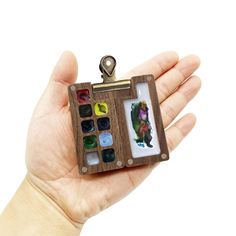 a hand holding a miniature photo frame with buttons in it's center and an image on the inside