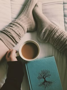 a person laying in bed with a book and cup of coffee