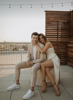 a man and woman sitting next to each other on top of a wooden bench in front of string lights