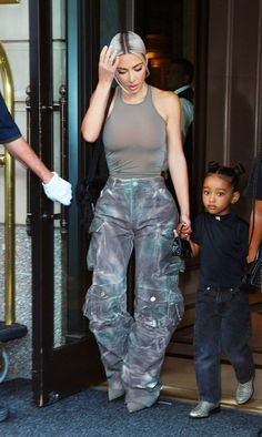 a woman in grey top and jeans walking with a small boy on the sidewalk next to an open door