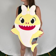 a woman holding up a cut out of a smiling yellow shark with big eyes and teeth