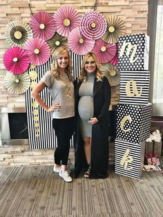 two pregnant women standing next to each other in front of paper flowers on the wall