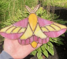 a hand is holding a stained glass humming bird ornament in front of some plants