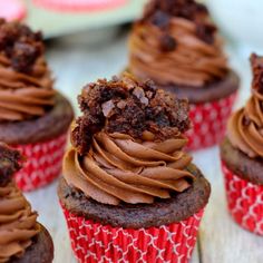 cupcakes with chocolate frosting on red and white paper wrappers sitting on a wooden table