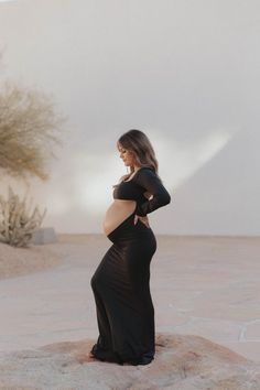 a pregnant woman in a black dress standing on a rock with her hands on her hips