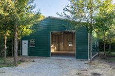 an empty garage in the middle of some trees and dirt area with one door open