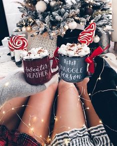 two cups of hot chocolate with marshmallows on them sitting next to a christmas tree