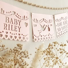 pink paper cutout cards hanging on a wall next to dried flowers and baby's breath