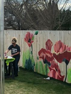 a woman sitting at a table in front of a fence with flowers painted on it