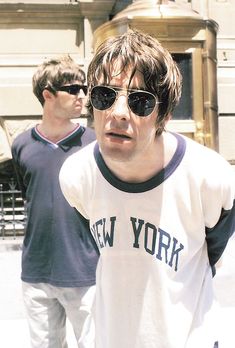 two young men walking down the street in front of a building, one with sunglasses on his head