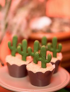 three cupcakes with green frosting and cactus decorations on them sitting on a plate