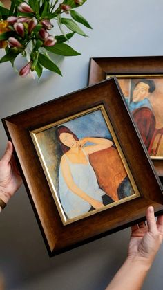 a woman holding two framed paintings in her hands