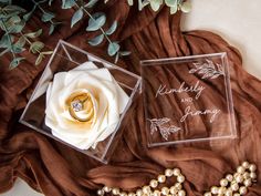 two wedding rings and a ring box on top of a brown cloth next to flowers