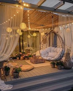 an outdoor area with hanging lights and furniture on the deck, surrounded by plants and flowers