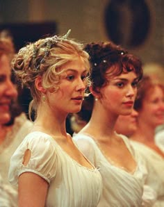 a group of women in white dresses standing next to each other and looking at the camera