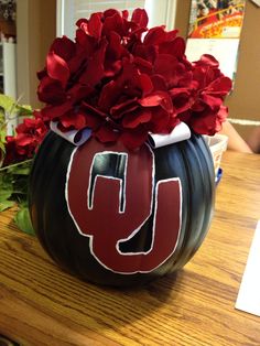 a black pumpkin with the letter u painted on it and red flowers in front of it