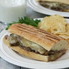 a plate with a sandwich and chips on it next to a glass of milk,