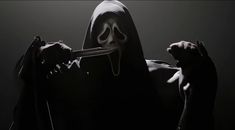 a person in a hooded costume holding a knife to their face with both hands and wearing a mask