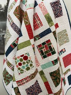 a close up of a colorful quilt on a white surface with trees in the background