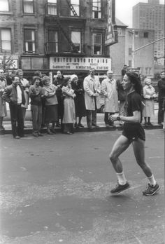 a woman is running in front of a group of people on the street and some are watching